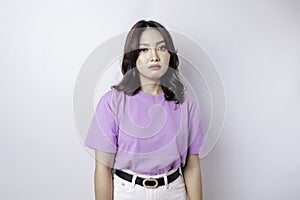 A portrait of an Asian woman wearing a lilac purple t-shirt isolated by white background looks depressed