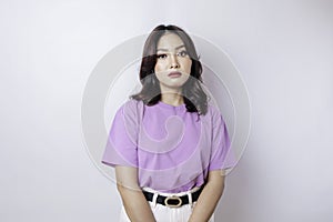 A portrait of an Asian woman wearing a lilac purple t-shirt isolated by white background looks depressed