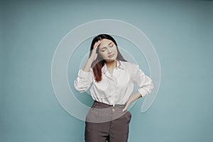 A portrait of an Asian woman wearing a white shirt isolated by blue background looks depressed