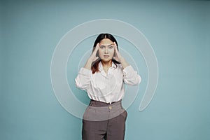 A portrait of an Asian woman wearing a white shirt isolated by blue background looks depressed