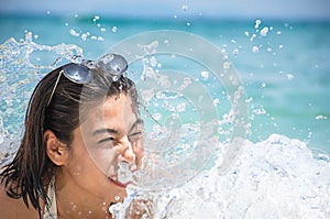 Portrait of Asian woman wearing white swimsuit and wear sunglasses lying on a sandy beach and water splashes