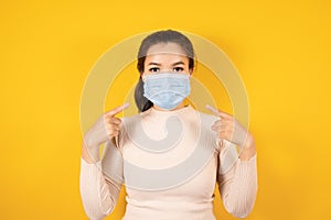 Portrait of Asian woman wears cream sweater and pointing a medical face mask to protect Covid-19