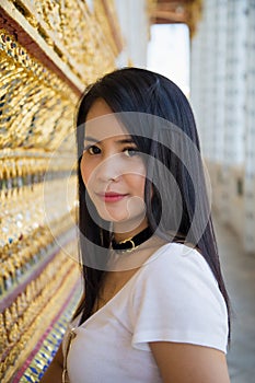 Portrait Asian woman in a white t-shirt standing next to a golden Thai tradition wall in The Buddhist temple photo
