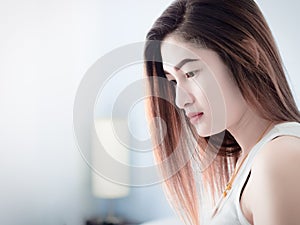 Portrait of Asian woman in white vest, on her bed, expressing the idea of broken heart and sadness. hopeless and await, concept.