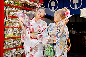 Portrait of Asian women wear japanese style dress with hold multicolor fan and stand in front of small shop and look happiness