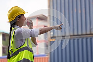 Portrait of Asian worker woman in safety uniform talking with walkie talkie to control work quality at container warehouse.