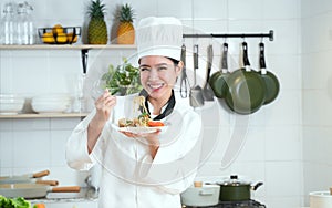 Portrait of Asian young beautiful chef woman wear white chef uniform and hat, holding spaghetti dish, smiling looking at camera