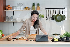 Portrait of Asian young beautiful woman standing in the kitchen and cooking healthy food with bread, fruits and vegetables.