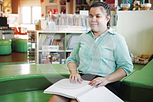 Portrait of Asian young blind woman disabled person reading Braille book in creative workplace