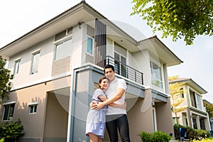 Portrait of Asian young couple standing and hugging together looking happy in front of their new house to start new life. Family,