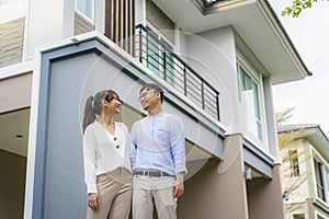 Portrait of Asian young couple standing and hugging together looking happy in front of their new house to start new life. Family,