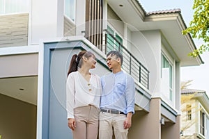 Portrait of Asian young couple standing and hugging together looking happy in front of their new house to start new life. Family,