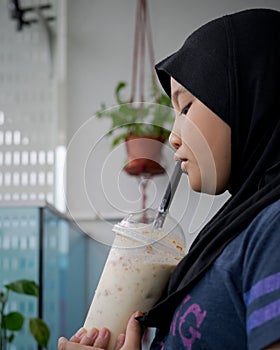 Portrait of Asian young girl wearing hijab drinking ice caramel blended in outdoor. Enjoying cold drink in hot season