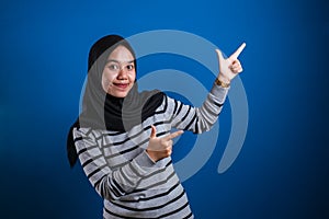 Portrait of Asian young happy asian muslim student girl smiling and pointing to presenting something on her side