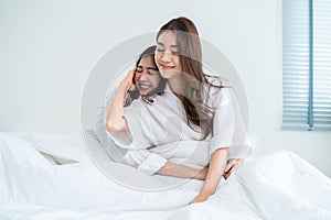 Portrait of Asian young lesbian couple sit on bed and hug each other. Attractive romantic girl friend in pajamas spending morning