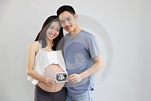 Portrait of asian young pregnant belly wife and asian husband holding ultrasound film with happiness and smile face on white