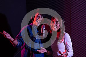 Portrait of asian young woman and man, artist singing into a microphone while recording a song in a studio