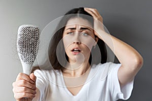 Portrait of a astonished caucasian young woman shows her hairbrush with losing hair. Gray background. The concept of