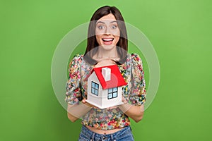 Portrait of astonished girl toothy smile hands hold little house isolated on green color background