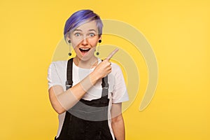 Portrait of astonished surprised fashionable hipster girl pointing to the side freespace for advertising. studio shot