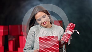 Portrait astonishment woman in sweater opening gift box with desired surprise posing at gray studio