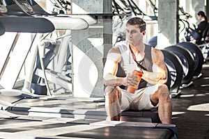 Portrait of athlete handsome masculine man sitting during treadmill exercise in gym, tired sportsman drinking water in sports hall