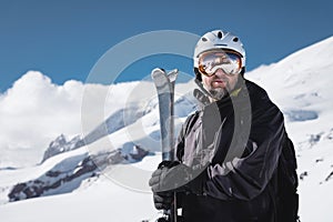 Portrait athlete skier in helmet and ski mask against the snow-capped mountains of a ski resort with a reflection of the