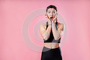 Portrait of athletic attractive muscular girl fitness trainer that shows excitement, worry, fright in the studio on the pink