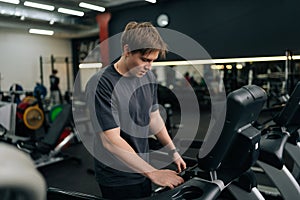 Portrait of athletic man in activewear adjusting settings on treadmill, preparing for cardio session in well-equipped