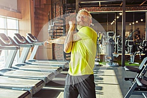 Portrait of athletic middle aged man in sportswear doing stretching exercises, warming up before workout in a gym or