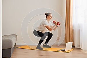 Portrait of athletic woman with hair bun doing squat, lower body sport exercise, keeping balance, warming up and training muscles