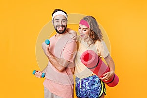 Portrait of athletic young couple holding dumbbells and fitness mat