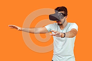 Portrait of attentive gamer, brunette man stretching arms forward while playing virtual reality game. isolated on orange