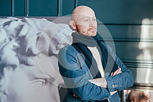 Portrait of attractive adult successful bald man art critic historian with beard in scarf in art gallery