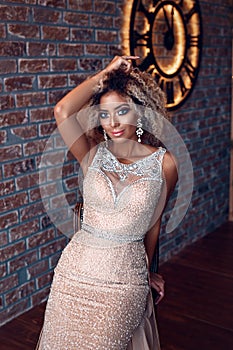 Portrait of attractive afro american young woman in tight gold dress in a luxury apartment. Beauty and fashion concept