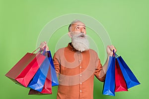 Portrait of attractive amazed cheerful grey-haired man holding buyings looking up wow isolated over green color photo