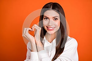 Portrait of attractive amorous cheerful girl showing heart sign 14 February isolated over bright orange color background