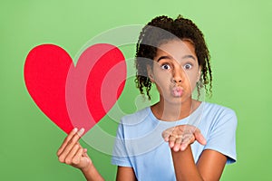 Portrait of attractive amorous girl holding big large heart sending air kiss  over green pastel color background