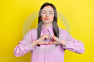 Portrait of attractive amorous girl sending air kiss showing heart sign isolated over bright yellow color background