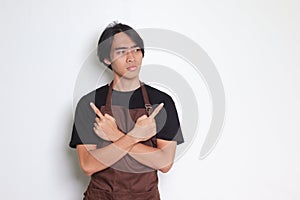 Portrait of attractive Asian barista man in brown apron showing product, pointing up right and left, showing two option of choices