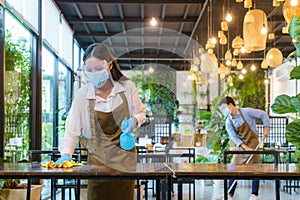 Portrait attractive Asian restaurant employee wear face mask and face shield cleaning table and floor with alcohol and wet wipe