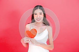 Portrait of attractive Asian smiling woman holding red heart paper jigsaw isolated on pink red background.