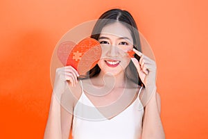 Portrait of attractive Asian smiling woman holding red heart paper jigsaw on pink red background.