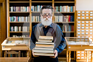 Portrait of attractive bearded old man wearing shirt and leather vest, high school teacher or librarian, holding books