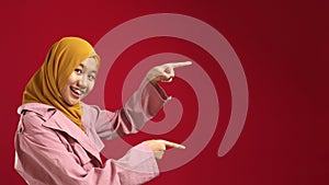 Portrait of attractive beautiful muslim teenage girl wearing hijab  smiling and pointing to the side with copy space, presenting