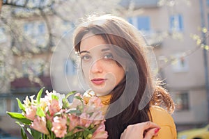 Portrait of attractive and beautiful young woman in yellow jacket holding a big bouquet of colorful flowers outdoors