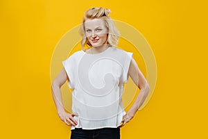 Portrait of an attractive blonde woman with hands on her waist over yellow