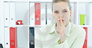 Portrait of an attractive business woman with finger on lips. Young businesswoman in office asking for silence.