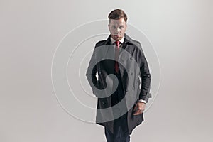 Portrait of attractive businessman in suit holding hand in long coat`s pocket