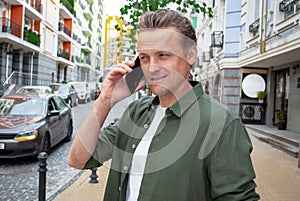 Portrait of an attractive businessman talking on smartphone at city street. Man ordered taxi for trip to office on